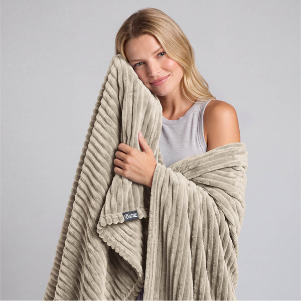 A woman is standing and holding a microplush blanket