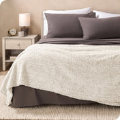 A textured sherpa blanket draped over the end and side of a bed