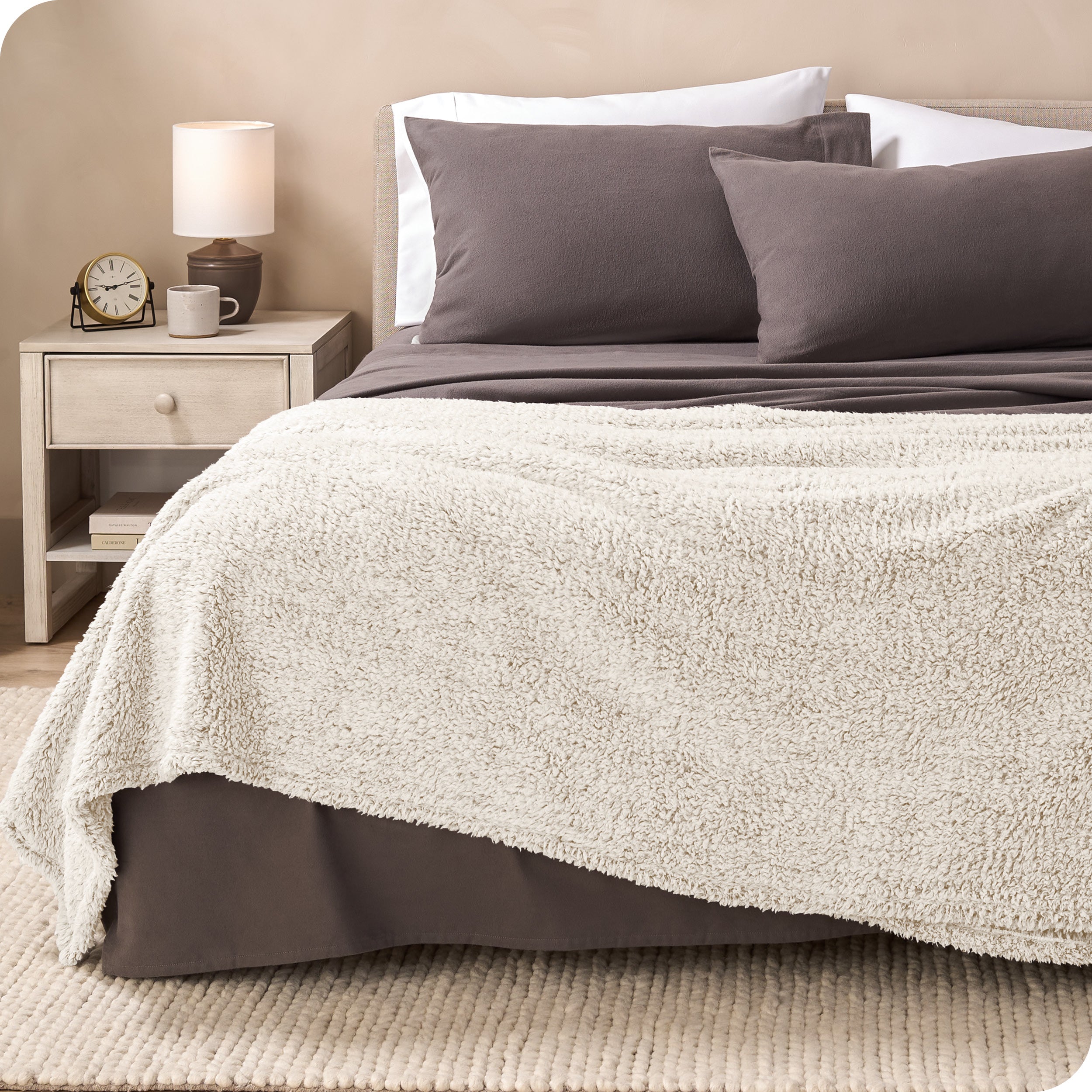 A textured sherpa blanket draped over the end and side of a bed