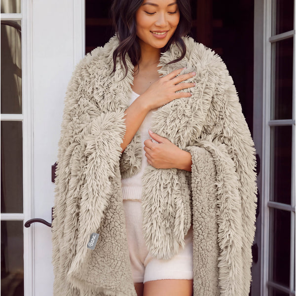 A woman standing with a shaggy blanket wrapped around her