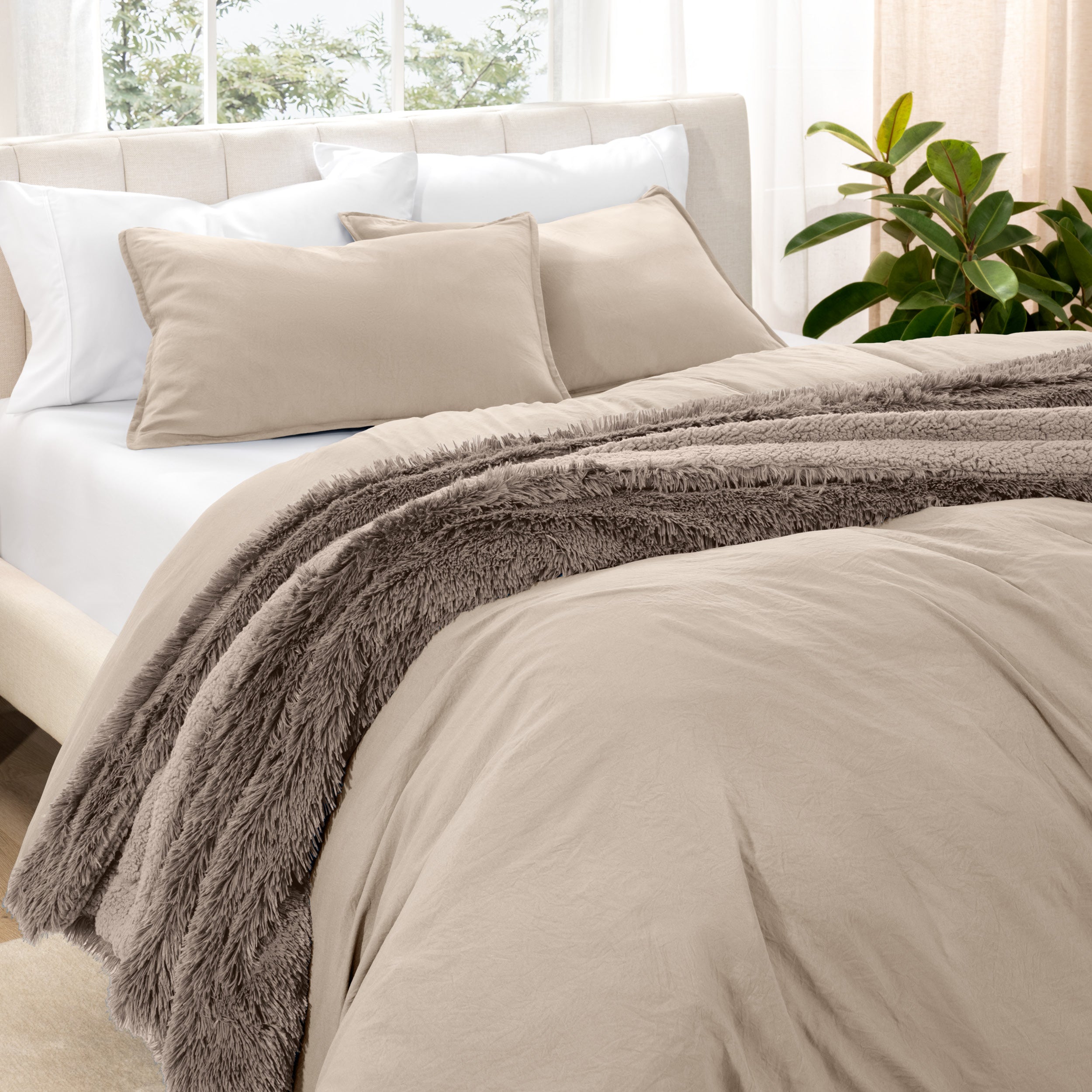 Washed bedding set on a bed in a bedroom with plants and nightstands.