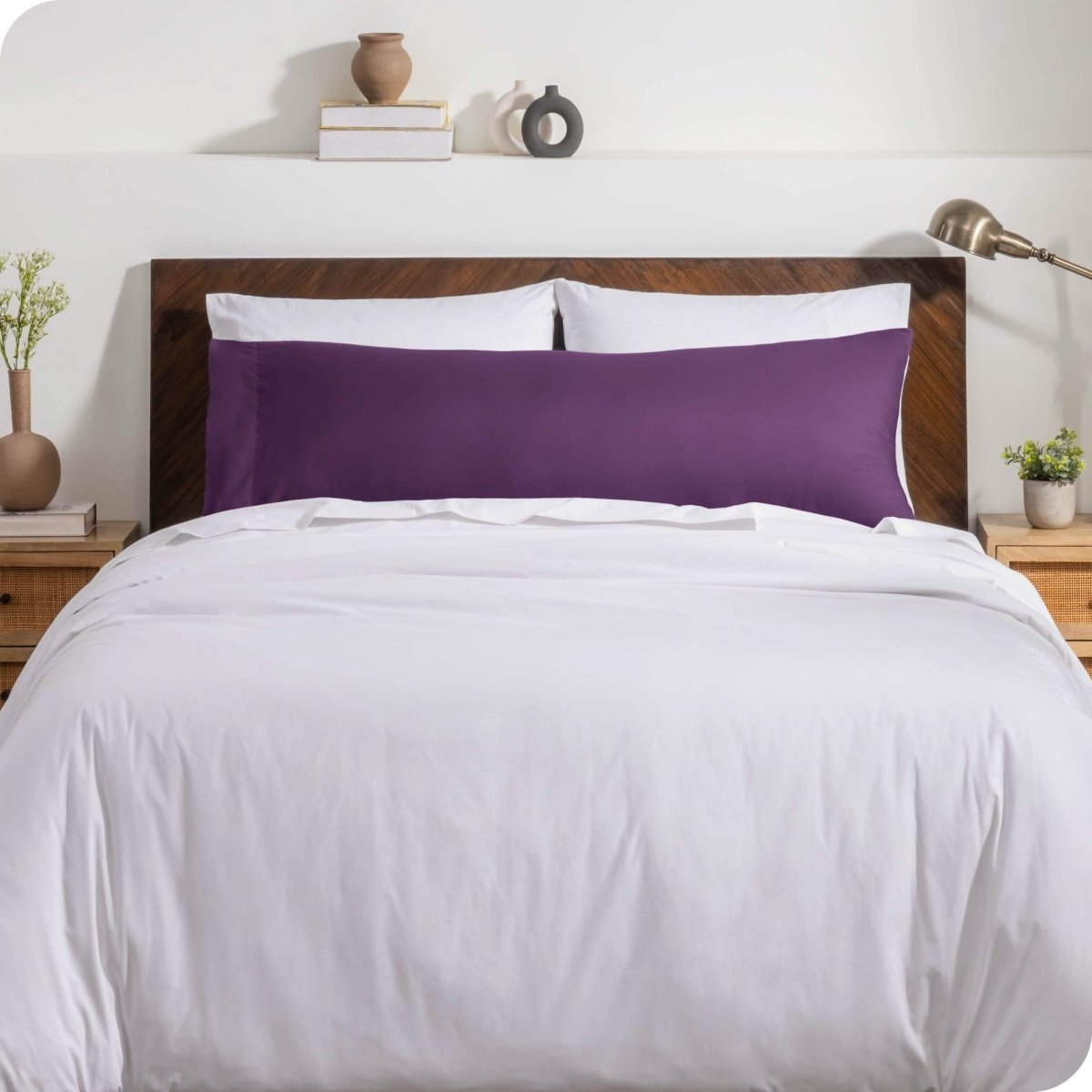 A body pillow cover on a pillow on a bed with other pillows and a duvet cover