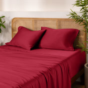 Bamboo bed sheets and pillows on a bed with a wicker headboard and plants in the background.