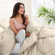 Woman sitting on a bed under duvet cover with a plant in the background