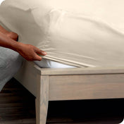 A man is kneeling while putting a fitted sheet on a mattress