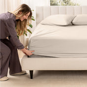 A woman is putting a fitted sateen sheet on a mattress