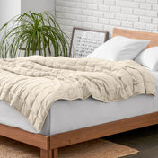 Weighted blanket on a bed with white pillows and a wooden headboard in a room with a plant and brick wall.