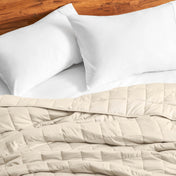 Cotton weighted blanket on a bed with white pillows against a wooden headboard.