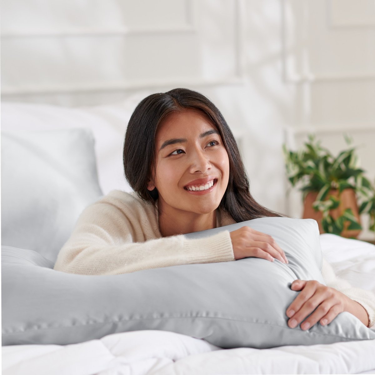 Woman lying on a bed with a body pillow, smiling.