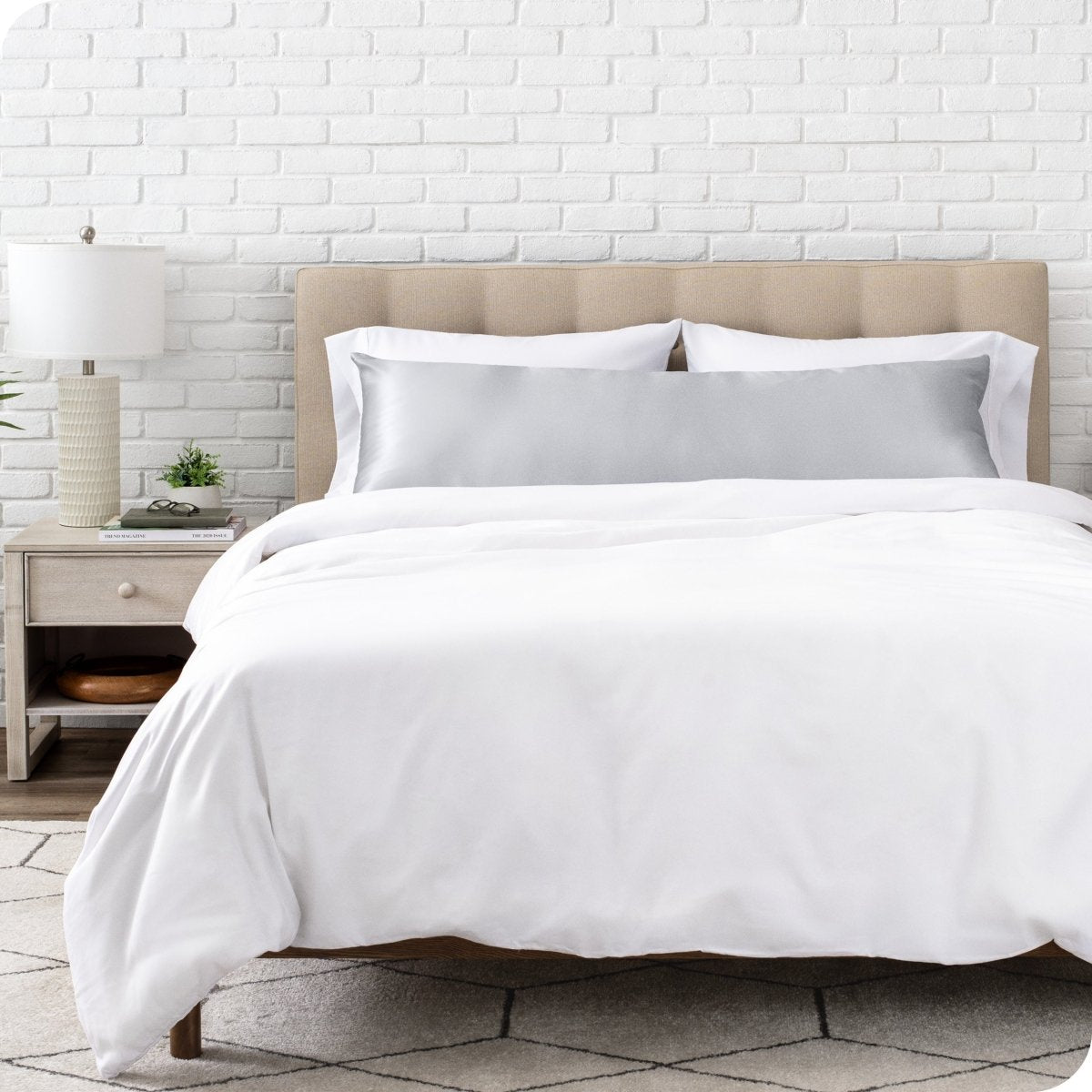Bed with white bedding and satin pillowcase against a white brick wall.