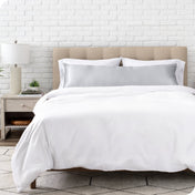 Bed with white bedding and satin pillowcase against a white brick wall.