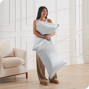A woman is standing and holding 2 pillows covered with silk pillowcases