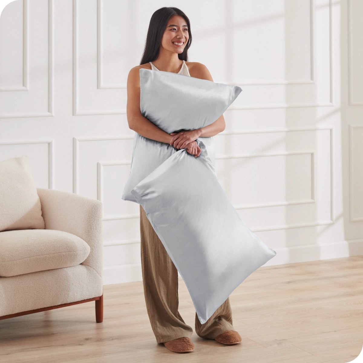 A woman standing while holding pillows with silk pillowcases on them