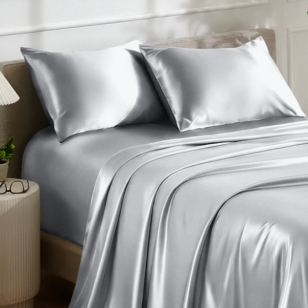 Satin bedding set on a bed with a nightstand and lamp in the background.
