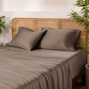 Bamboo bed sheets and pillows on a bed with a wicker headboard and plants in the background.