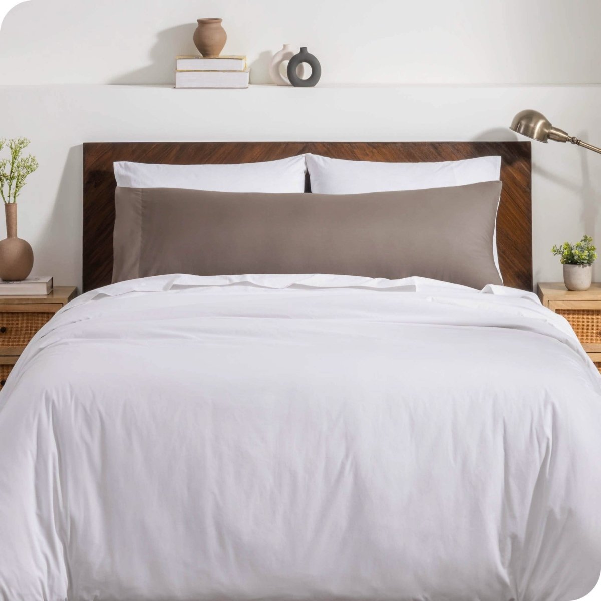 A body pillow cover on a pillow on a bed with other pillows and a duvet cover