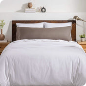A body pillow cover on a pillow on a bed with other pillows and a duvet cover