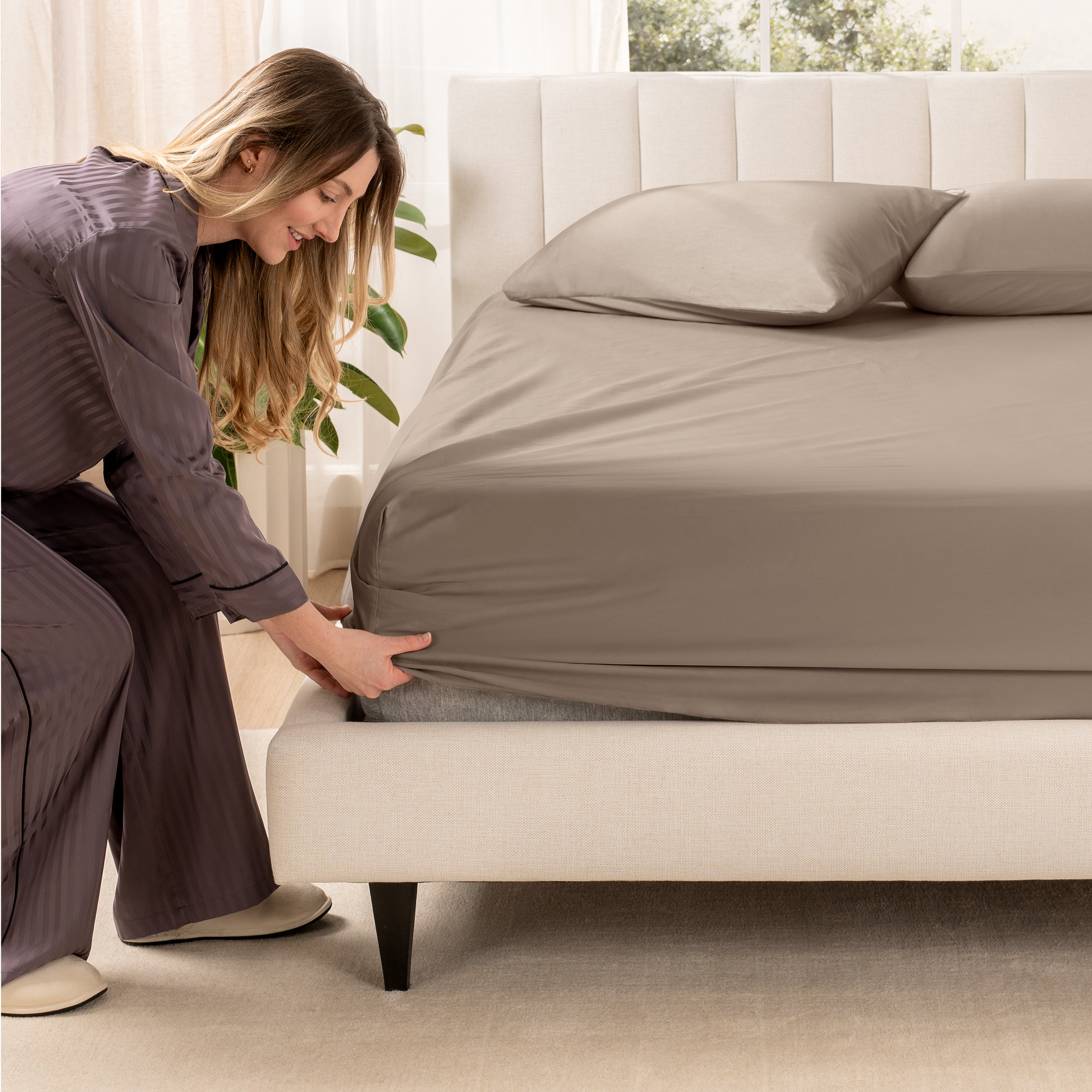 A woman is putting a fitted sateen sheet on a mattress
