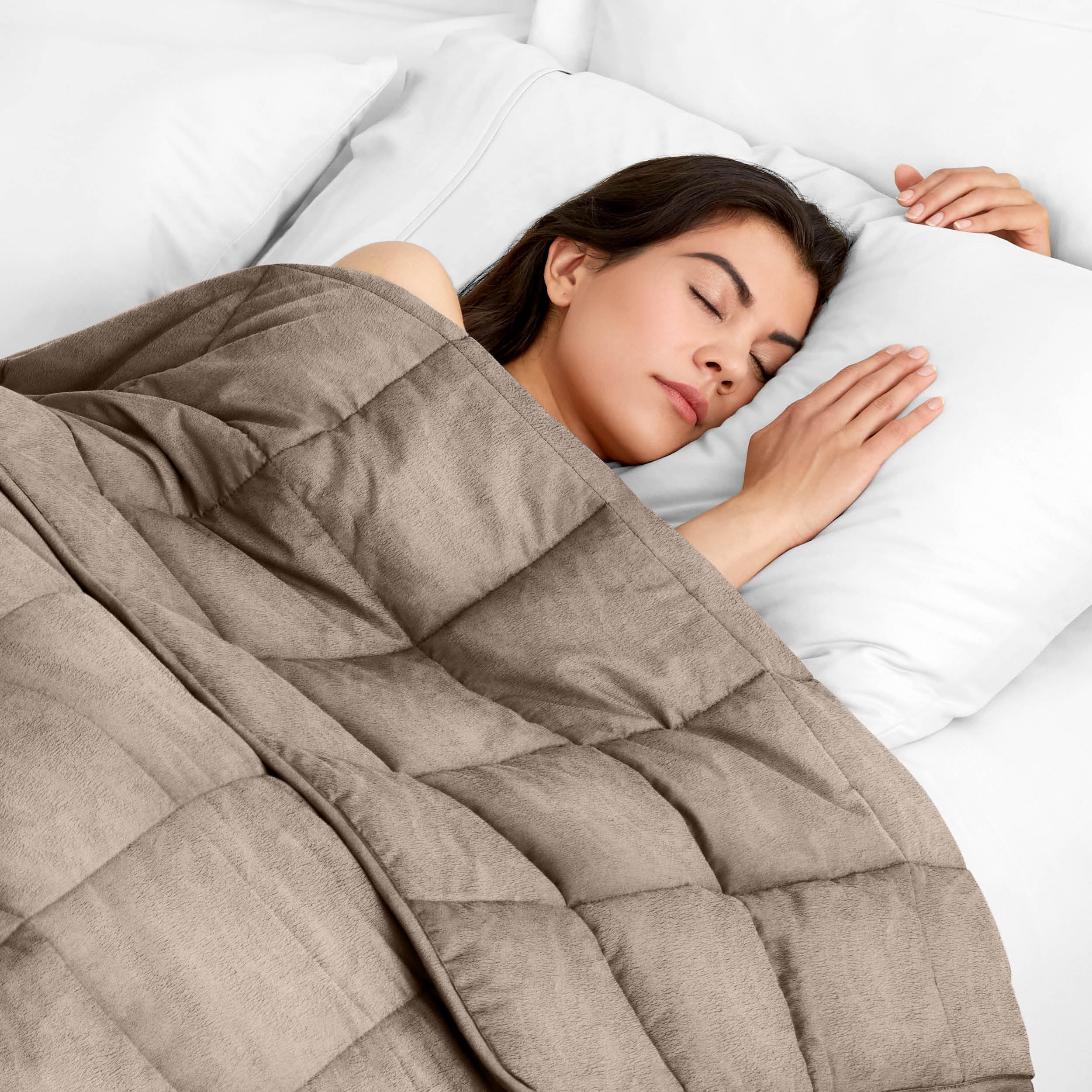 Woman sleeping peacefully under a weighted blanket with white pillows