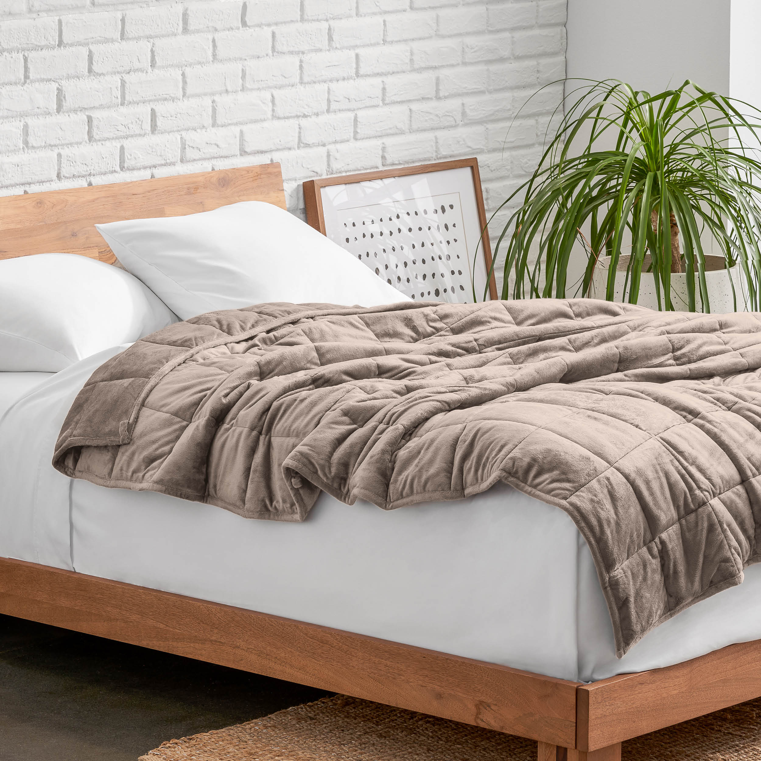 Weighted blanket on a bed with white pillows and a wooden headboard in a room with a plant and brick wall
