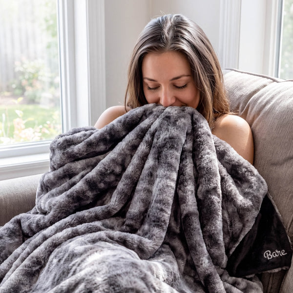 A woman sitting on a couch with a faux fur blanket wrapped around her.