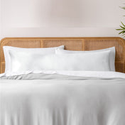 Pillows, sheets and a duvet cover on a bed with a wicker headboard and light gray bedding.