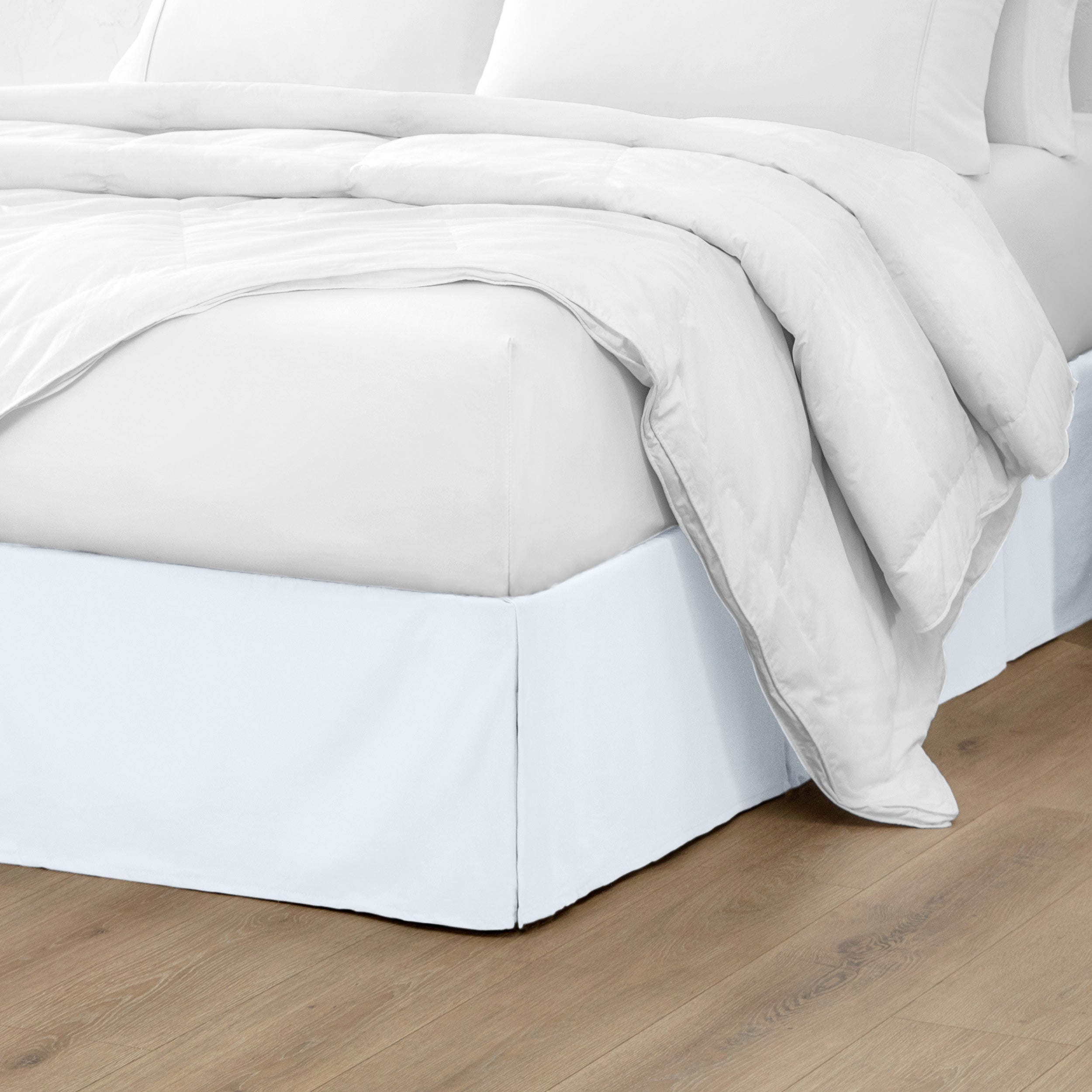 A modern bed with a microfiber bed skirt with pleats on the corners and midway on each side
