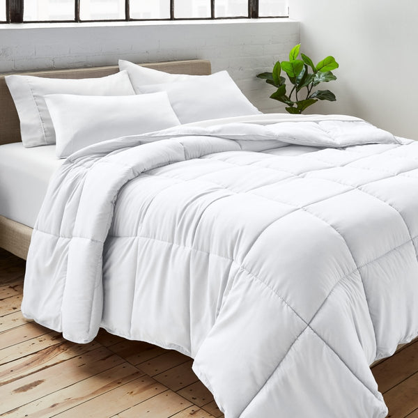 Comforter on a bed with white pillows and a plant in the corner.
