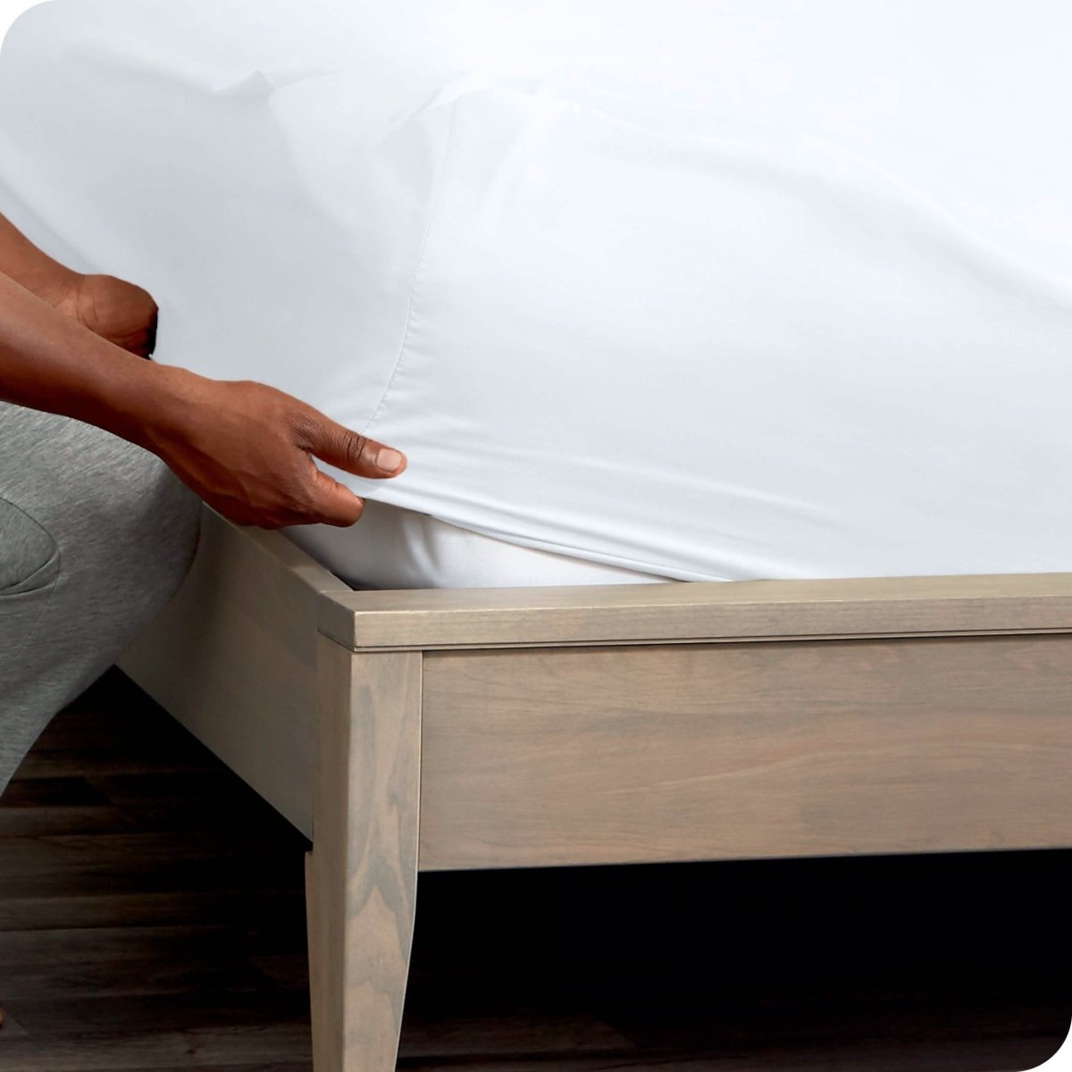 A man is kneeling while putting a fitted sheet on a mattress