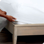 A man is kneeling while putting a fitted sheet on a mattress