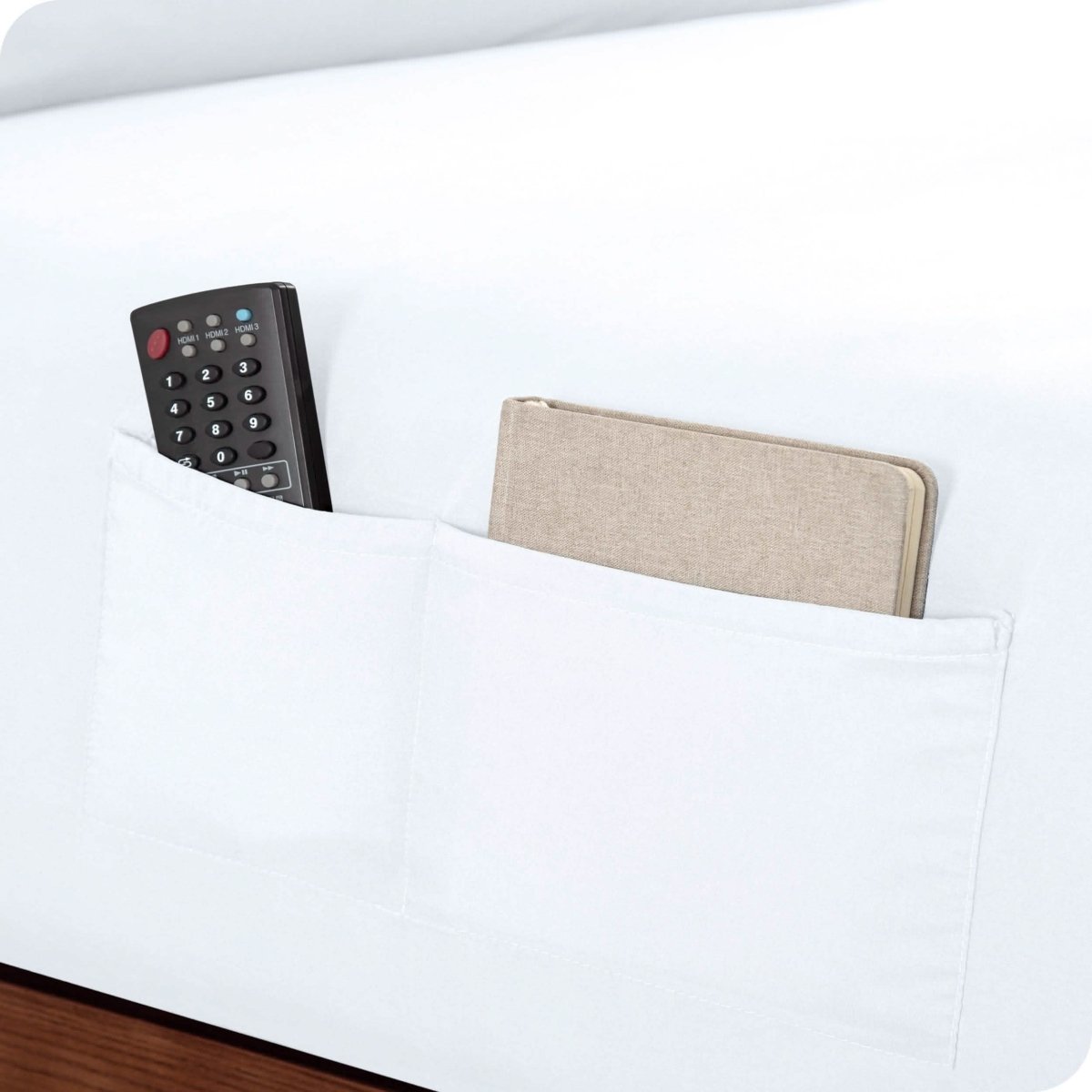 Close up of 2 pockets on a fitted sheet with a remote and journal in the pockets