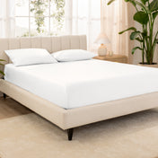 A bed made with an organic cotton sateen fitted sheet and matching pillowcases on pillows