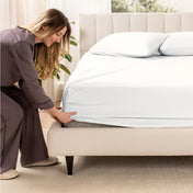 A woman is putting a fitted sateen sheet on a mattress