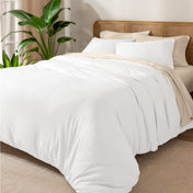 A cozy bed dressed in white sheets and pillows, complemented by an organic cotton jersey duvet cover set.