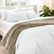 Washed bedding set on a bed in a bedroom with plants and nightstands.