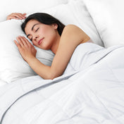 Woman sleeping peacefully under a weighted blanket with white pillows