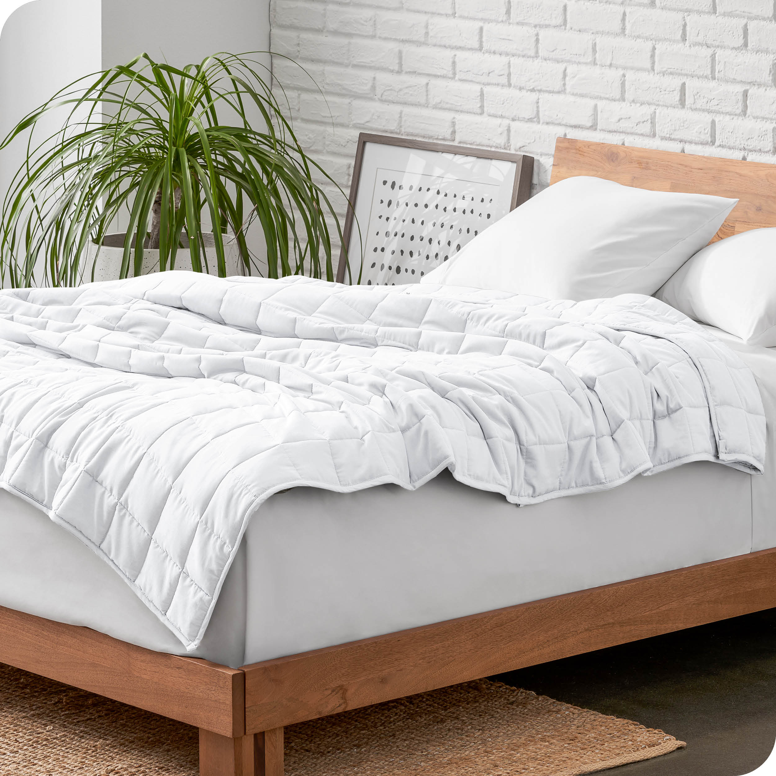Weighted blanket on a bed with white pillows and a wooden headboard in a room with a plant and brick wall.