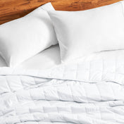 Cotton weighted blanket on a bed with white pillows against a wooden headboard.