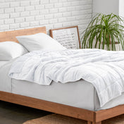 Weighted blanket on a bed with white pillows and a wooden headboard in a room with a plant and brick wall