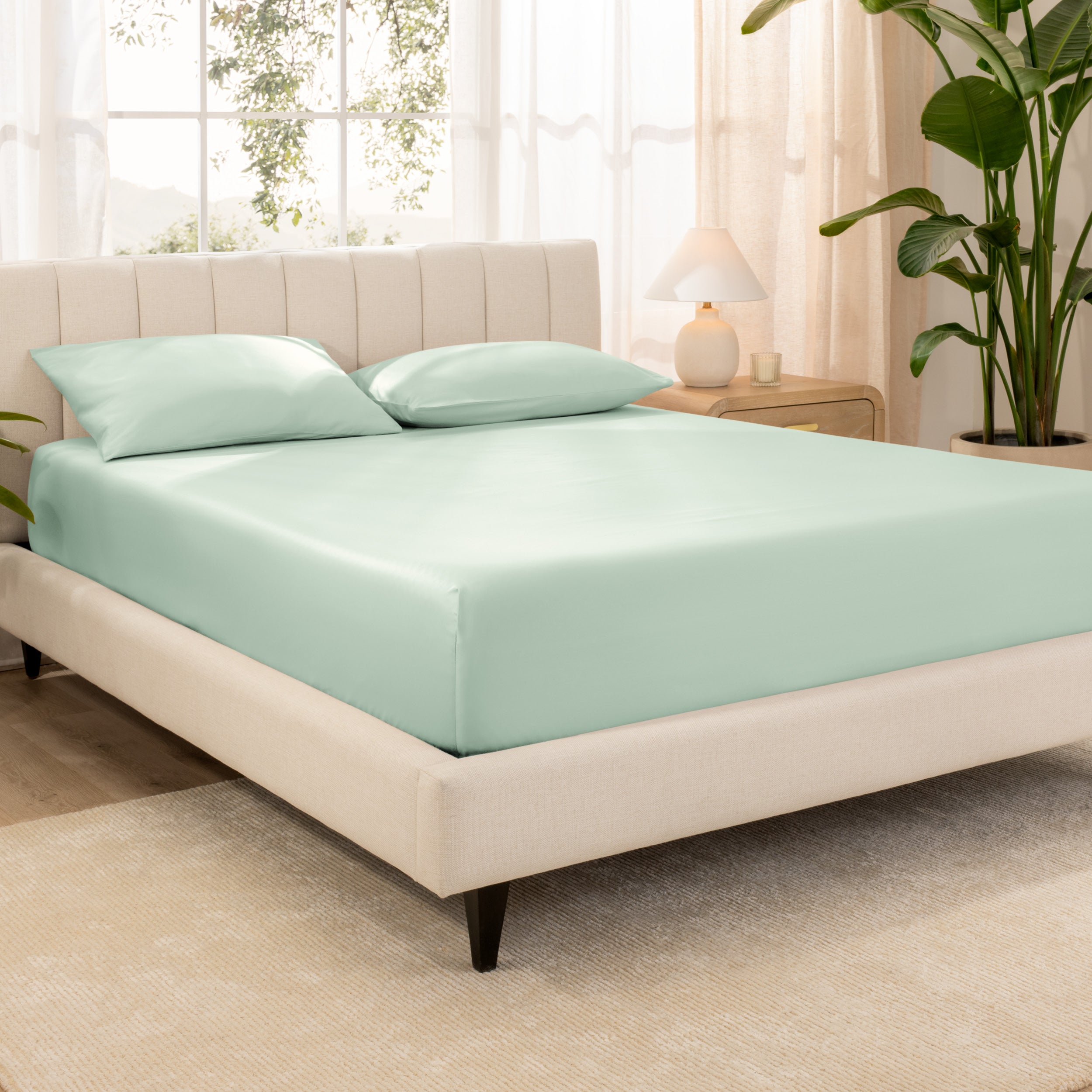 A bed made with an organic cotton sateen fitted sheet and matching pillowcases on pillows