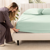 A woman is putting a fitted sateen sheet on a mattress