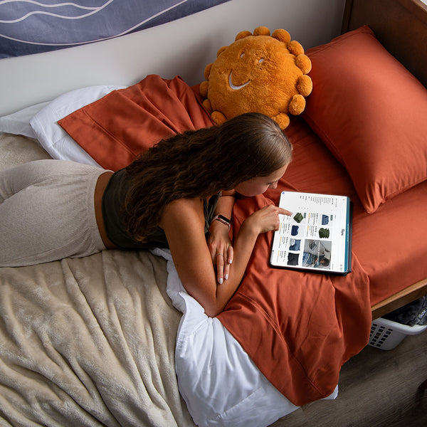 Young college woman browsing bare homes website site on a terracotta colored bed