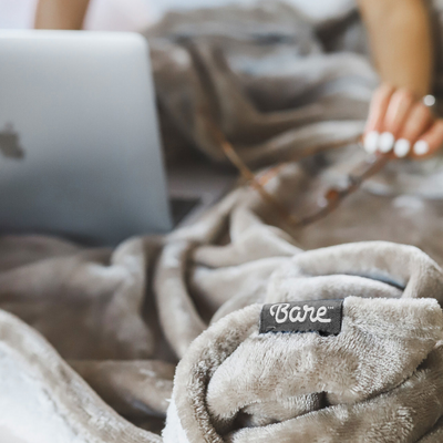 Closeup of a phone resting on a grey blanket with a Bare Home tag
