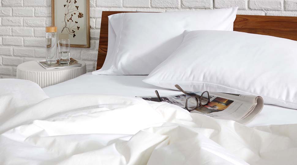 A room scene with a bed dress in all white. A magazine and a pair of glasses are on the bed.