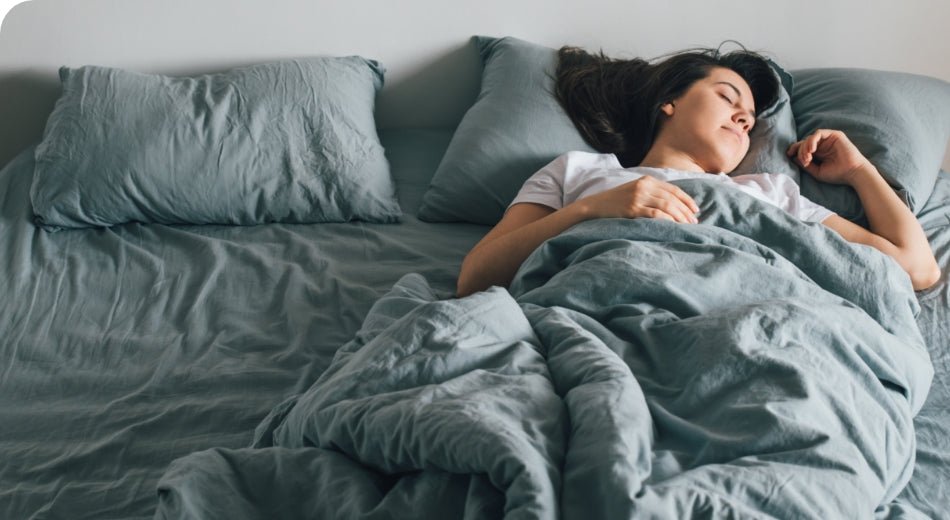 A woman is sleeping on her back with head resting on a pillow. The sheets and comforter are green.