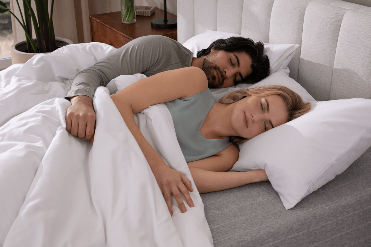 A man and woman sleeping on their sides in bed