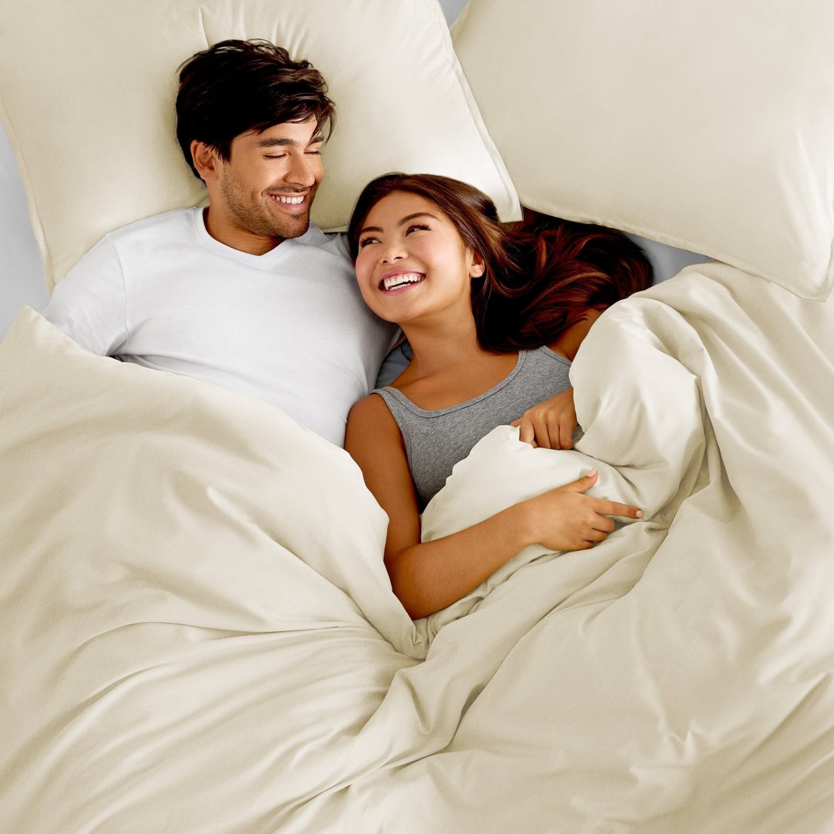 Man and a woman laying in bed beneath a tan colored duvet