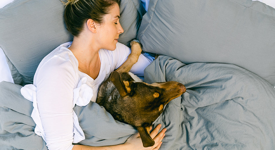 A woman sleeps in bed while cuddling her dog.