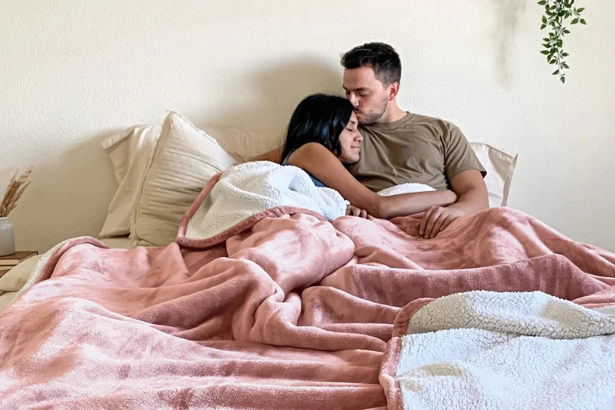 A happy couple sitting in bed together under a pink blanket 