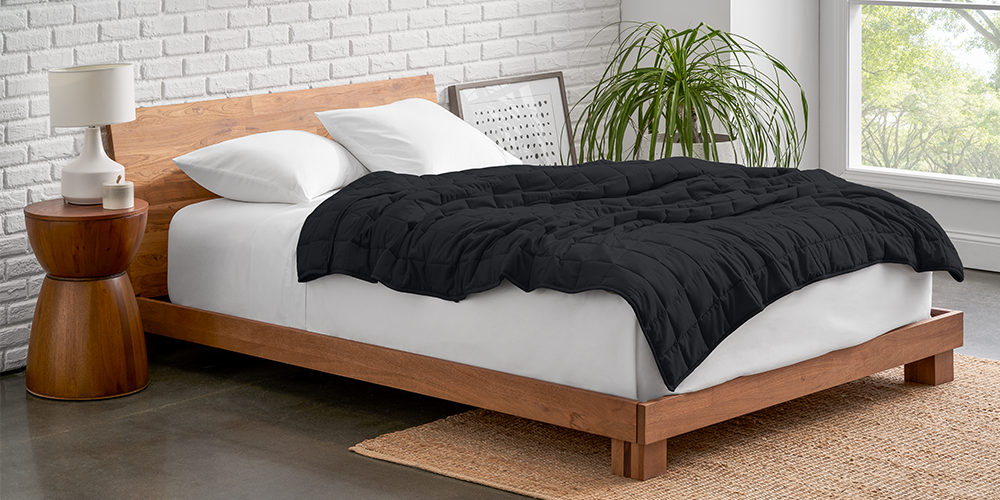 Bed with a white weighted blanket next to a wood nightstand